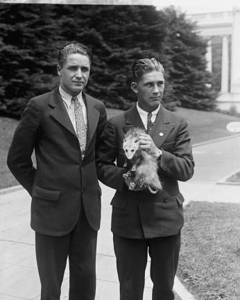 A man and a high school student on the grounds of possibly the White House, holding Billy the possum