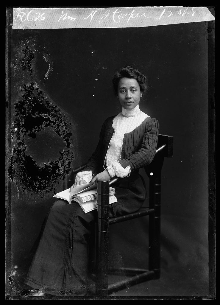 A black-and-white photograph of Anna Julia Cooper seated in a photo studio with a book on her lap