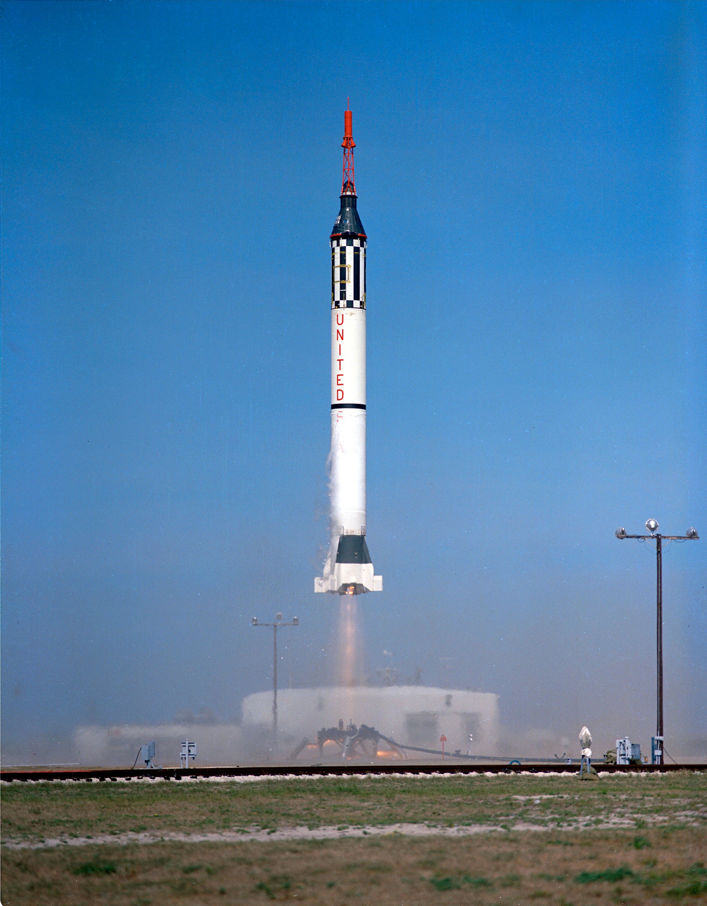 Color photo of NASA rocket lifting off from launch pad on with clear blue skies.