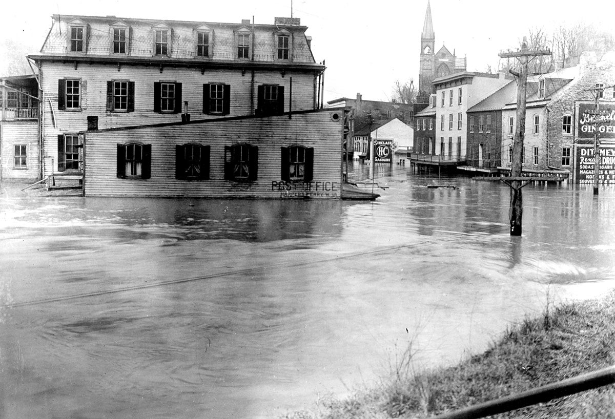 A photograph of Harper Ferry with water covering the bottom half of the wood and brick buildings