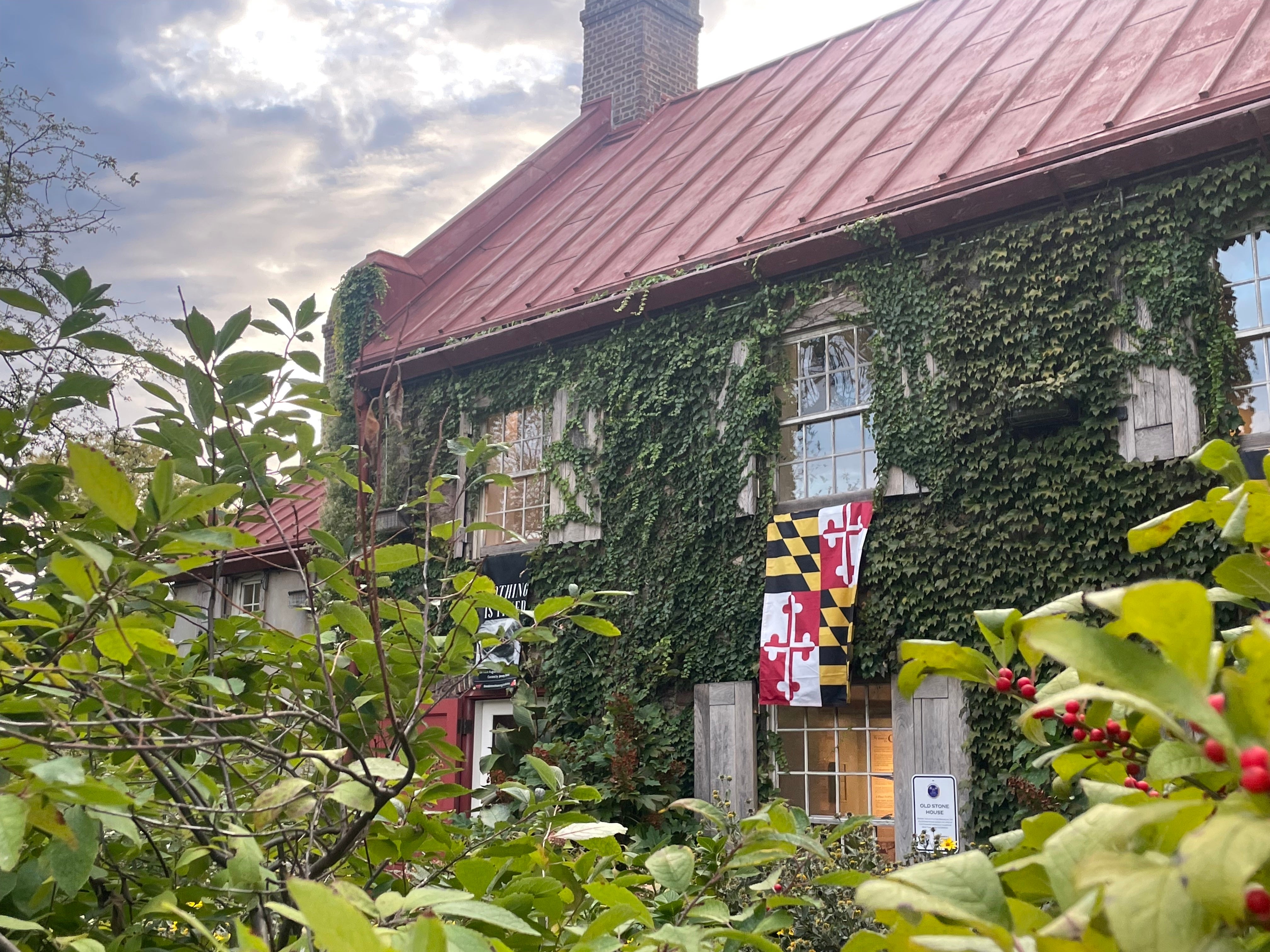 Stone house with ivy growing on the walls and a Maryland flag hanging from window.