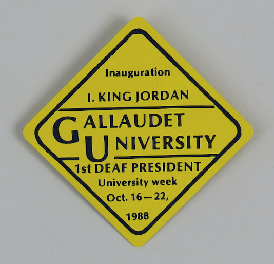 DPN Button Image of a yellow diamond-shaped button commemorating the inauguration of I. King Jordan. Text on the button reads: Inauguration I. King Jordan, Gallaudet University, 1st Deaf President, University Week October 16-22 1988.