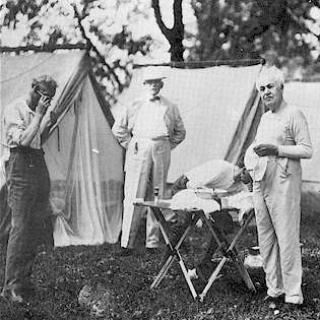 Henry Ford, Bishop William F. Anderson, Harvey Firestone (stooping). Thomas A. Edison and President Warren G. Harding pose as they shave in the morning