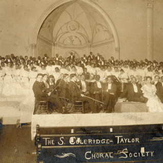 The Samuel Coleridge-Taylor Choral Society, a chorus of around 200 people, posing with orchestra and composer Samuel Coleridge-Taylor at a concert in 1906. 