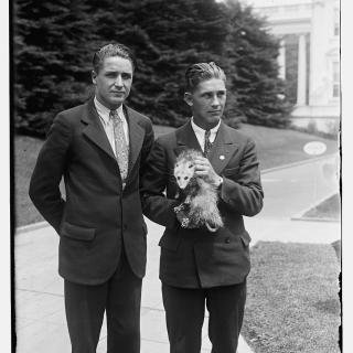 A man and a high school student on the grounds of possibly the White House, holding Billy the possum