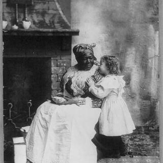 Picture of a seated black "mammy" listening to a small white girl. Source: Library of Congress