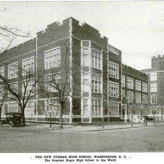 Streetview image of Dunbar High School circa 1917. Castle-like red brick and stone trimmed structure with cars parked on left side.