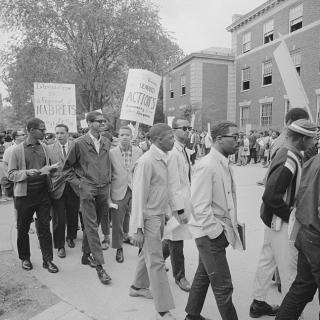 Crowd looks on as group of Howard University students on university campus protest holding picket signs.