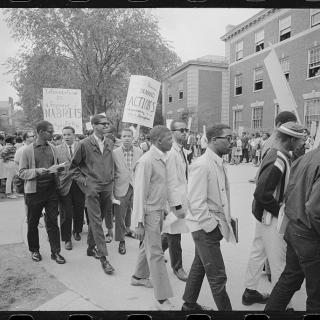 Crowd looks on as group of Howard University students on university campus protest holding picket signs.