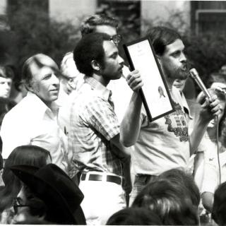 Maccubbin, Wilson, and Kameny stand at the stage to read the D.C. City Council's proclamation at Gay Pride Day 1975. (Source: Rainbow History Project)