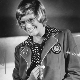 Melissa Belote holding gold medal and wearing Olympic jacket.