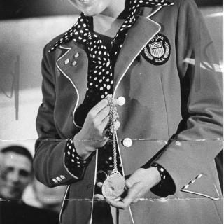 Melissa Belote holding gold medal and wearing Olympic jacket.