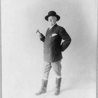 Black and white portrait of Edward Payson Weston looking at the camera holding a cane and wearing a double breasted suit jacket, mid-calf length boots, and a wide brim hat.