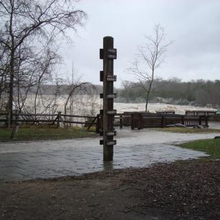 A large wooden pole with various years attached at differing heights in front of a flooded river