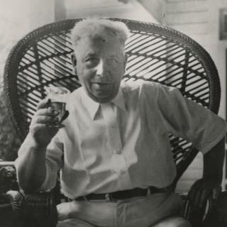 An older man holds up a drink to the camera.