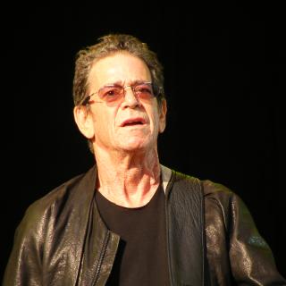White man with glasses playing guitar. 