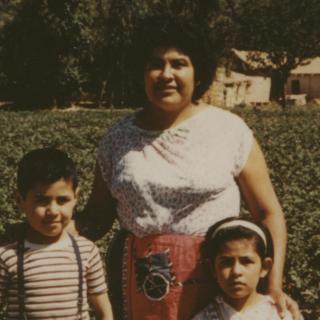 Latino mother stands with young boy and young girl.