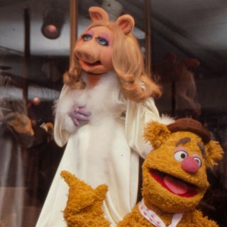 Jim Henson dressed in white suit standing with Miss Piggy and Fozzie Bear