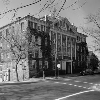 Black and white photo of large brick house with cars in front.