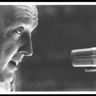An up close shot of Grant talking into a microphone (1960).