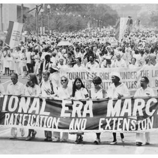 A group of demonstrators march with a large banner reading "National ERA March for Ratification and Extension" in their hands