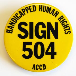 Bright yellow protest button created by the American Coalition of Citizens with Disabilities (ACCD). The pin reads in black block-lettering: "Handicapped Human Rights, Sign 504, ACCD." [Source: National Museum of American History]