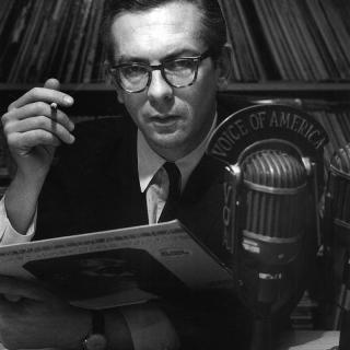A young and serious Willis Conover, cigarette in one hand, jazz record in the other, in his Voice of America studio. Source: Wikimedia Commons