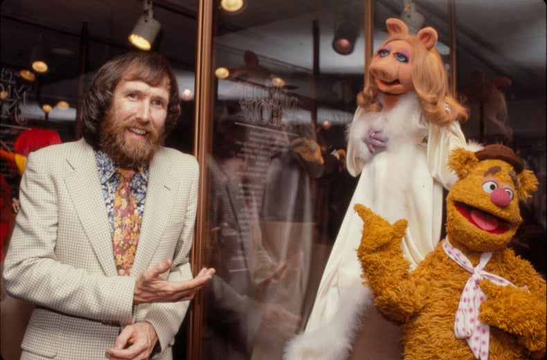 Jim Henson dressed in white suit standing with Miss Piggy and Fozzie Bear