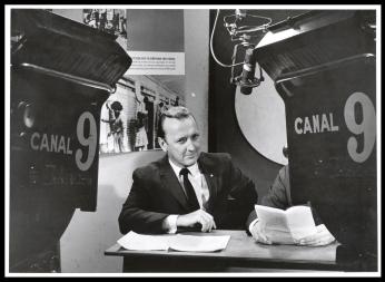 Grant sits at a desk in a newsroom. He is sharply dressed with a suit and tie. He looks intently at someone or something not captured in the picture. Grant sits at a desk in a newsroom. He is sharply dressed with a suit and tie. He looks intently at someone or something not captured in the picture.