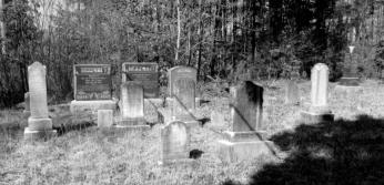 A black and white photograph of a cemetery. About ten medium-sized tombstones are visible.