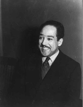 A black-and-white photo of Langston Hughes wearing a suit and smiling against a dark background