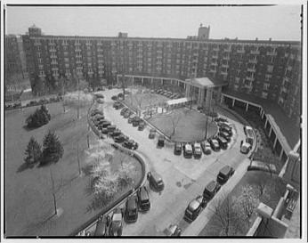 A black-and-white aerial photo of the Wardman-Park hotel, showing the 8-story building in a semi-circle around a roundabout where many cars are parked, and a grassy area with blooming trees