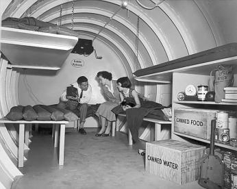 Black and white photo of parents and young daughter sitting on bunk beds in family fallout shelter.