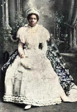 A black woman in a dress, cape, and crown