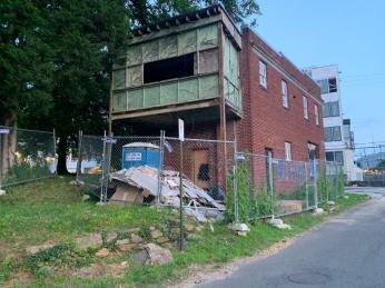 A dilapidated brick house on a corner. It is surrounded by a metal fence. (Source: Mary-Kate Wilson)