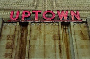 A close-up of red capital letters spelling UPTOWN on a building facade. The sign is worn down and there is grime on the building. (Alex Barth from Washington DC, USA, CC BY 2.0 <https://creativecommons.org/licenses/by/2.0>, via Wikimedia Commons)