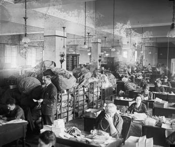 Employees sitting in Dead Letter office surrounded by piles of mail and mail bags. (Source: Library of Congress)