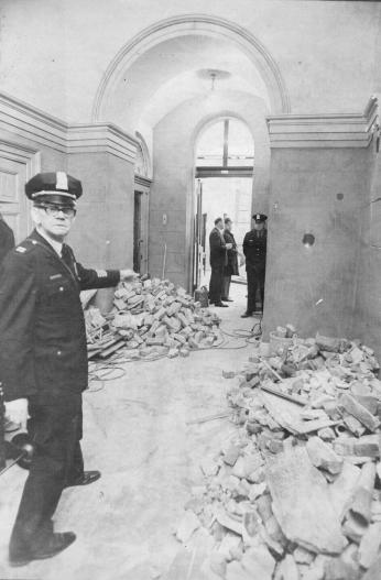 Capitol Police officer stands in a damaged hallway with rubble visible.