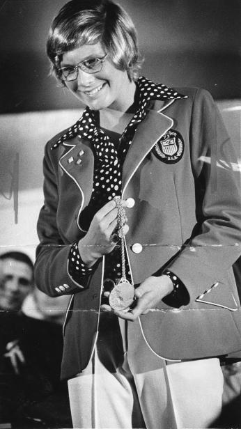 Melissa Belote holding gold medal and wearing Olympic jacket.