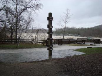A large wooden pole with various years attached at differing heights in front of a flooded river