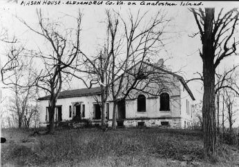 Old white house on hilltop. Trees without leaves stand in front of the house.