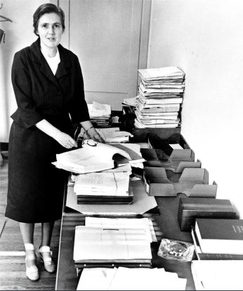 Dr. Frances O. Kelsey, full-length portrait, standing, facing front, in her office at the Food and Drug Administration, next to table with reports on new drugs she has been unable to process since her involvement in refusing to license the drug Thalidomide