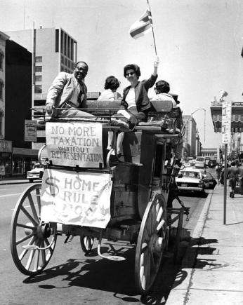 William Porter and Helen Leavitt sit on the back of a stagecoach, showing a banner that reads, "Taxation Without Representation."