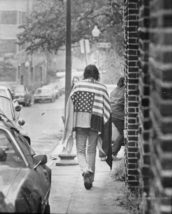 Man walking with his back to the camera with American flag draped over his shoulders