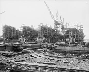 Metal shipbuilding material in the foreground with four large vessels in construction in the background.