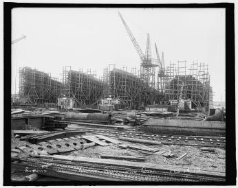 Metal shipbuilding material in the foreground with four large vessels in construction in the background. 