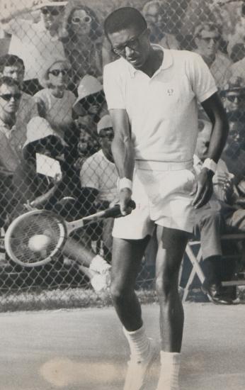 Arthur Ashe hitting a tennis ball with his racket during a match.