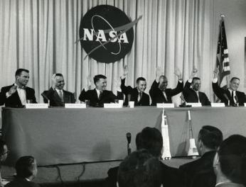 “The Mercury 7 astronauts (left to right) Slayton, Shepard, Schirra, Grissom, Glenn, Cooper, and Carpenter all raise their hands in reply to a question about whether they felt confident they would return from space – Glenn raised both hands,” 1959 (Photo Source: NASA) <a href=