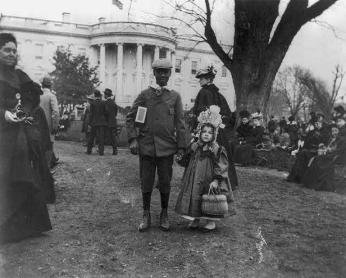 African American boy holding hand of small white girl during Easter egg roll