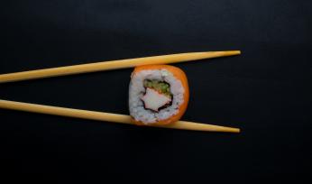 Chopsticks holding sushi roll. (Credit: Mahmoud Fawzy on Unsplash)
